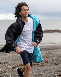 Boy running on a beach, wearing Black Blue dryrobe® Advance Kids Long Sleeve