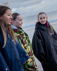 Three girls walking along a beach, wearing dryrobe® Advance Kids Long Sleeve
