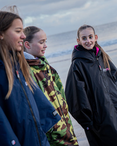 Three girls walking along a beach, wearing dryrobe® Advance Kids Long Sleeve