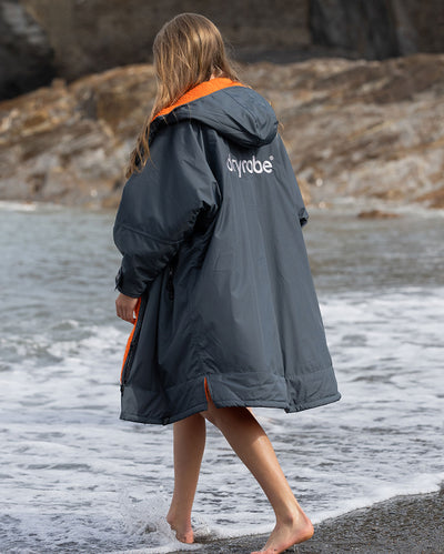 Girl walking along shore line on the beach wearing dryrobe AdvanceLong Sleeve Change robe in Dark Grey Orange
