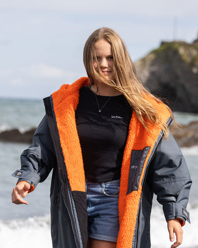 Girl walking on beach towards camera wearing dryrobe Advance Long Sleeve Change robe in Dark Grey Orange