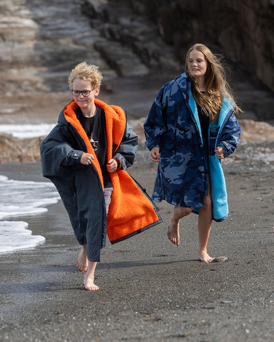 Boy and girl running together on a beach, wearing dryrobe Advance Long Sleeve Change robes 