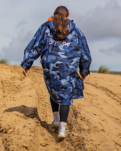 Girl walking up sand dune wearing dryrobe Advance Long Sleeve Changing robe in Blue Camo Orange