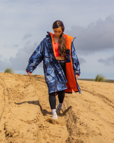 Girl walking down sand dune wearing dryrobe Advance Long Sleeve Changing robe in Blue Camo Orange