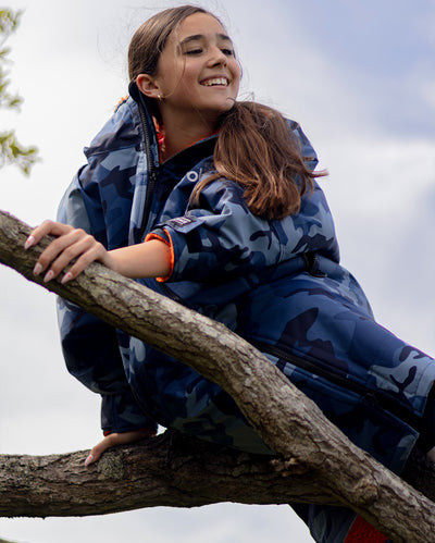 Girl smiling sat in tree, wearing dryrobe Advance Long Sleeve Changing robe in Blue Camo Orange