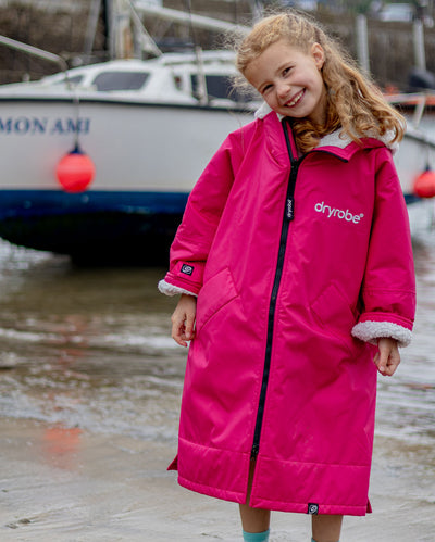 Girl smiling stood in front of boat, wearing dryrobe Advance Long Sleeve Changing robe in Pink Light Grey 