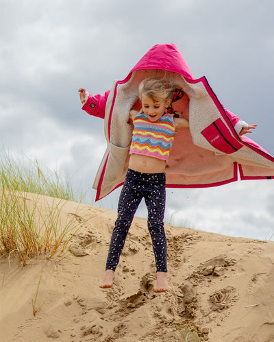 Girl jumping down sand dune, wearing dryrobe Advance Long Sleeve Changing robe in Pink Light Grey 