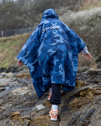 Girl climbing over rocks with back to the camera, wearing Blue Camo Kids dryrobe® Waterproof Poncho