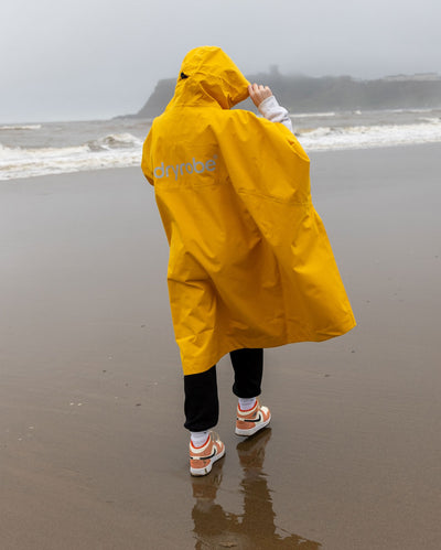 Girl walking away from camera on a beach, wearing Yellow Kids dryrobe® Waterproof Poncho