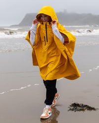 Girl smiling wearing Yellow Kids dryrobe® Waterproof Poncho, walking on a beach