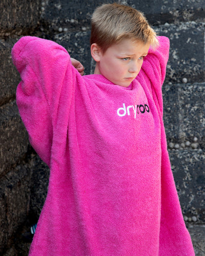 Boy stood in front of a wall, wearing Kids Towel Robe in Pink