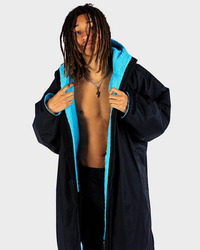 Person wearing a black dryrobe with blue lining on a white background