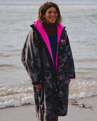 *MALE* dryrobe® Ambassador Siyanda Hewitt standing on a beach, wearing Black Camo Pink dryrobe® Advance Long Sleeve 