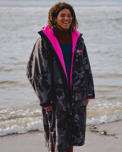 *MALE* dryrobe® Ambassador Siyanda Hewitt standing on a beach, wearing Black Camo Pink dryrobe® Advance Long Sleeve 