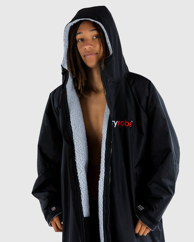 Person wearing a black dryrobe with grey lining and a visible brand logo on a white background