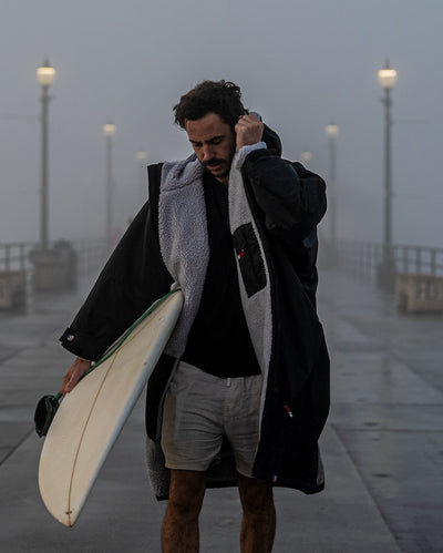*MALE* carrying surfboard walking towards camera in the rain, wearing Black Grey dryrobe® Advance Long Sleeve