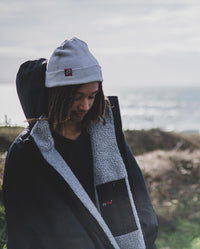 *MALE* stood in front of the sea, wearing Grey dryrobe® Eco Beanie and Black Grey dryrobe® Advance Long Sleeve