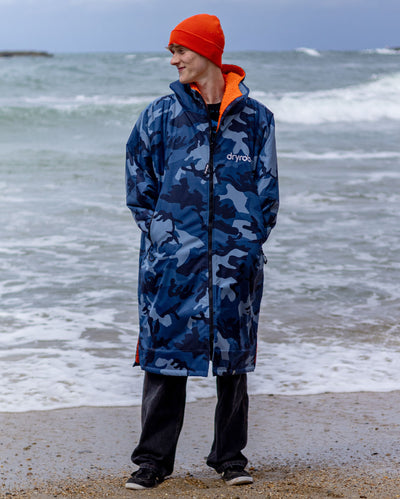 **MALE** Man stood in front of ocean wearing Blue Camo Orange dryrobe advance long sleeve changing robe and orange dryrobe beanie