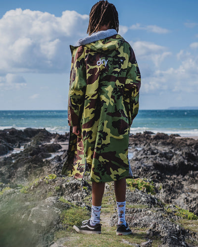*MALE* standing on a beach facing the sea, wearing Camo Grey dryrobe¬Æ Advance