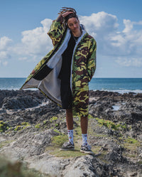 *MALE* facing the camera stood in front of the sea,  wearing Camo Grey dryrobe® Advance