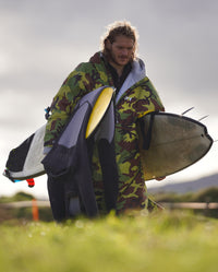 *MALE* carrying two surfboards with wetsuit draped over one, wearing Camo Grey dryrobe® Advance
