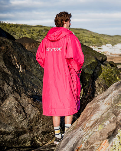 **MALE** Man stood with back to the camera on rocks wearing dryrobe Advance long sleeve changing robe in Pink Light Grey