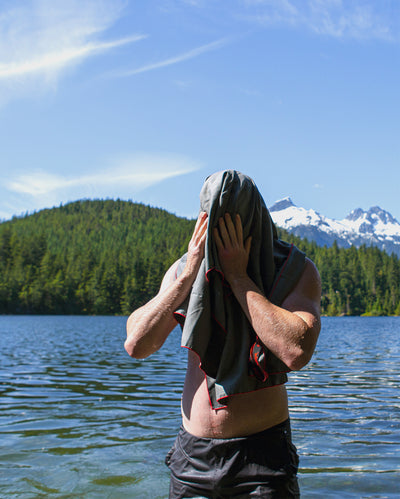 Man stood in lake, using dryrobe Microfibre Towel to dry face