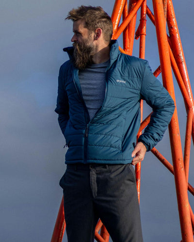 Man wearing dryrobe Mid-layer Jacket in Deep Sea Blue, with blue sky behind him
