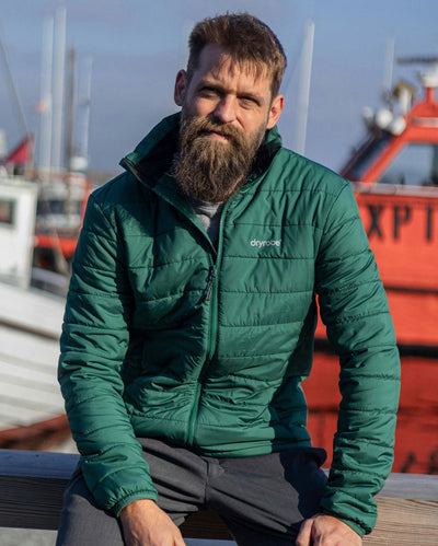 Man sat in sun in front of boats, wearing dryrobe Mid-Layer Jacket in Hunter Green 
