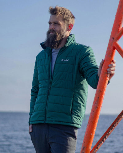 Man stood in sun in front of sea, wearing dryrobe Mid-Layer Jacket in Hunter Green 