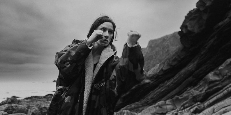 Person in a coat standing on rocky terrain with a dramatic sky