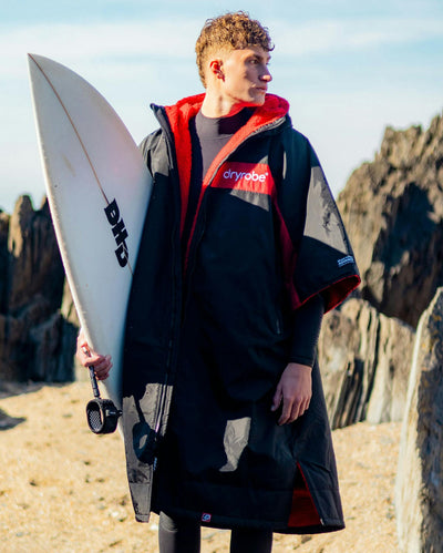 Adult male on beach wearing Dryrobe® Black red remix