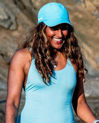 1|Woman smiling on a beach, wearing blue dyrobe® quick dry cap 