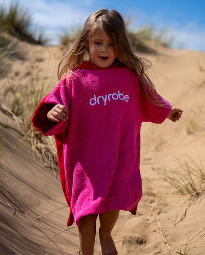 Child running down sand dune, wearing Kids Organic Towel dryrobe in Pink Red