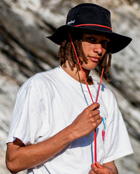1|Man wearing Black dryrobe® Quick Dry brimmed hat, holding orange adjustable chin strap 